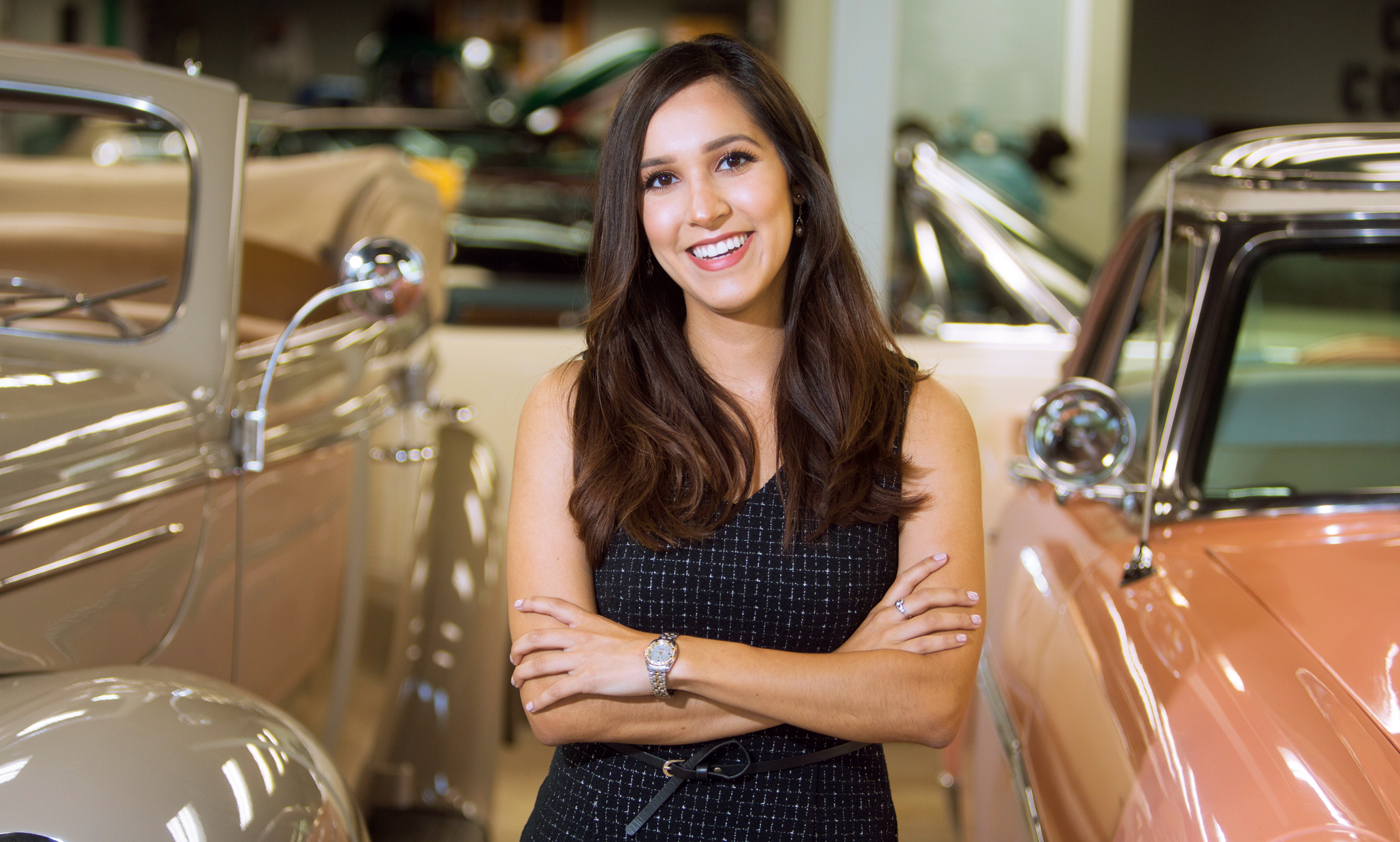 Vreni Fernandez standing by classic cars at the Kansas City Auto Museum